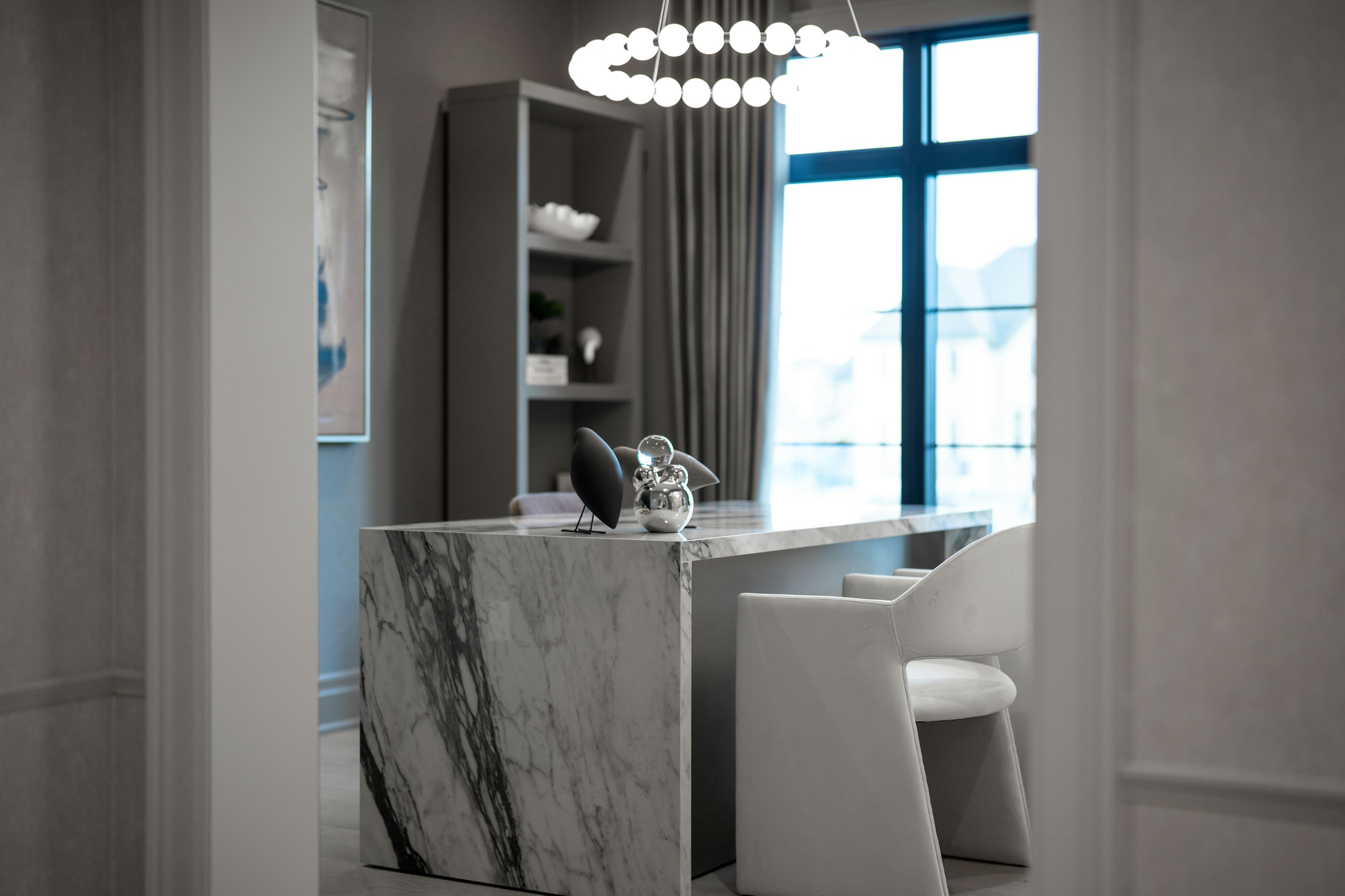 A modern private office with a sculptural marble desk, upholstered chairs, and a large window